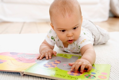 Baby boy lying on floor with picture book, touching page with his hands, front view